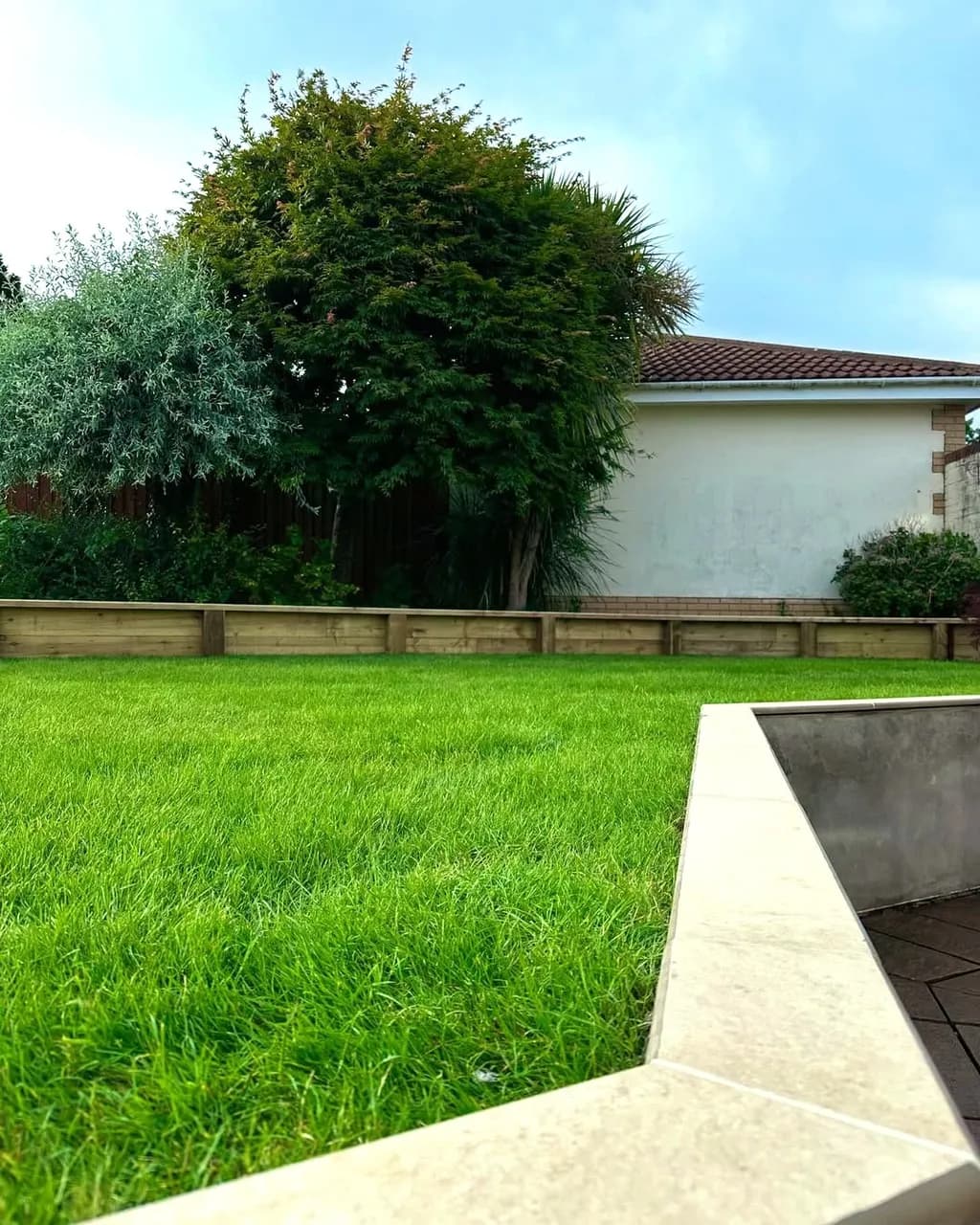 Tiered garden transformation in Cwmbran with treated sleeper retaining wall, levelled ground, and freshly laid turf.