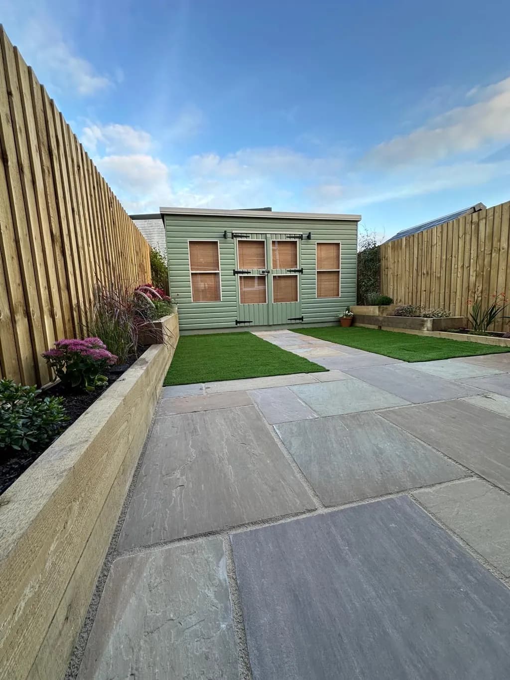 Tiered wooden sleeper planters creating raised levels in the garden beside an Indian sandstone patio.