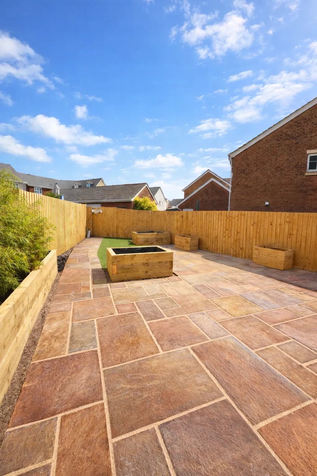 Artificial grass area bordered by sandstone paving and timber sleeper planters.