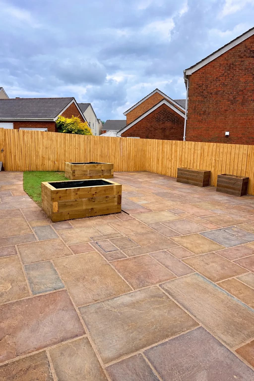 Wide view of an Indian sandstone patio with new fencing and wooden planters in the background.
