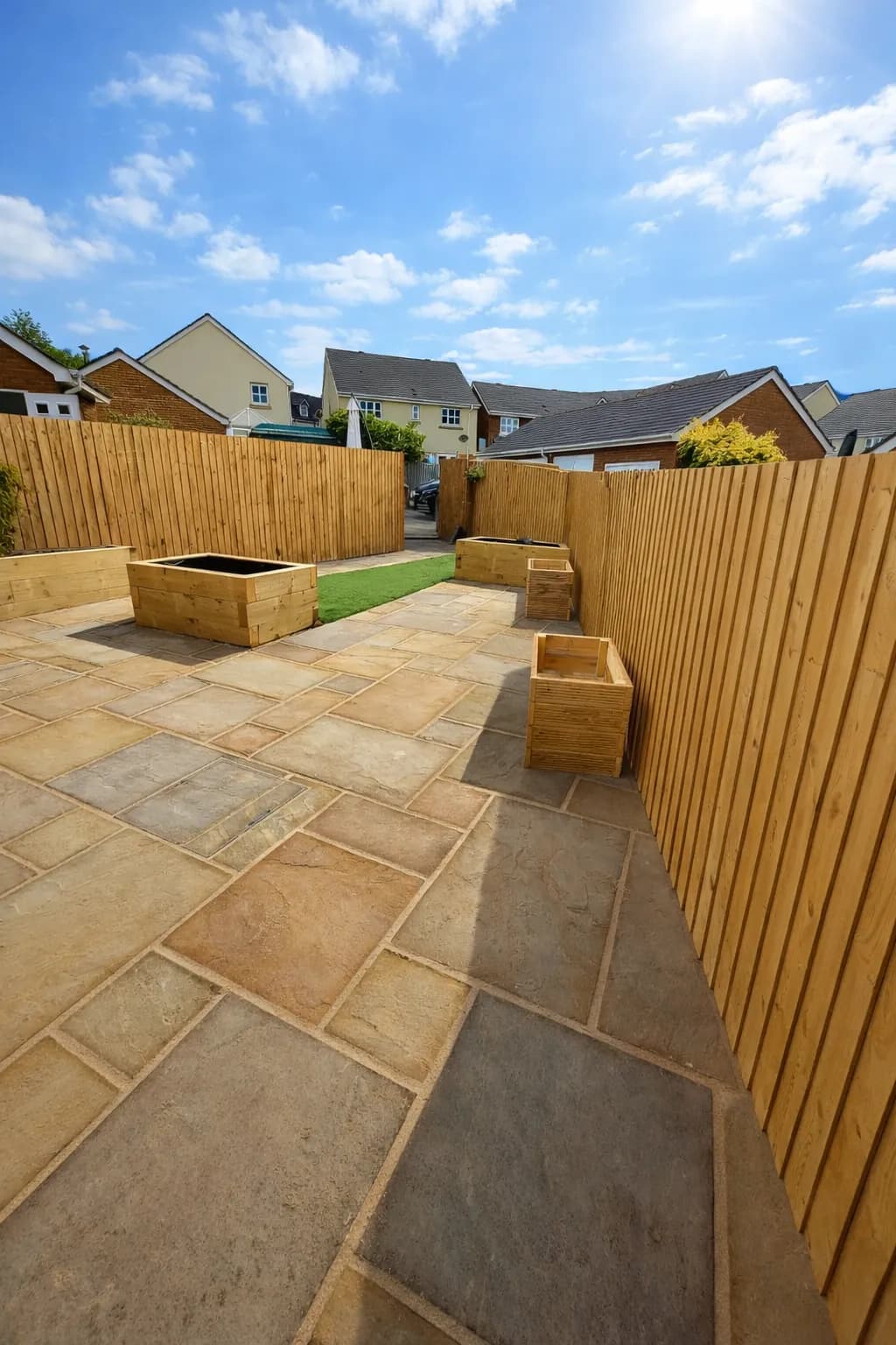 Indian sandstone patio with light timber fencing and raised sleeper planters.