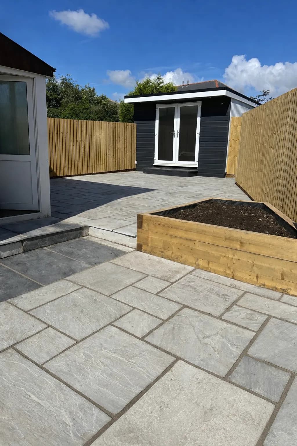 Raised sleeper bed and newly laid turf alongside Indian sandstone pathway at side of residential property.