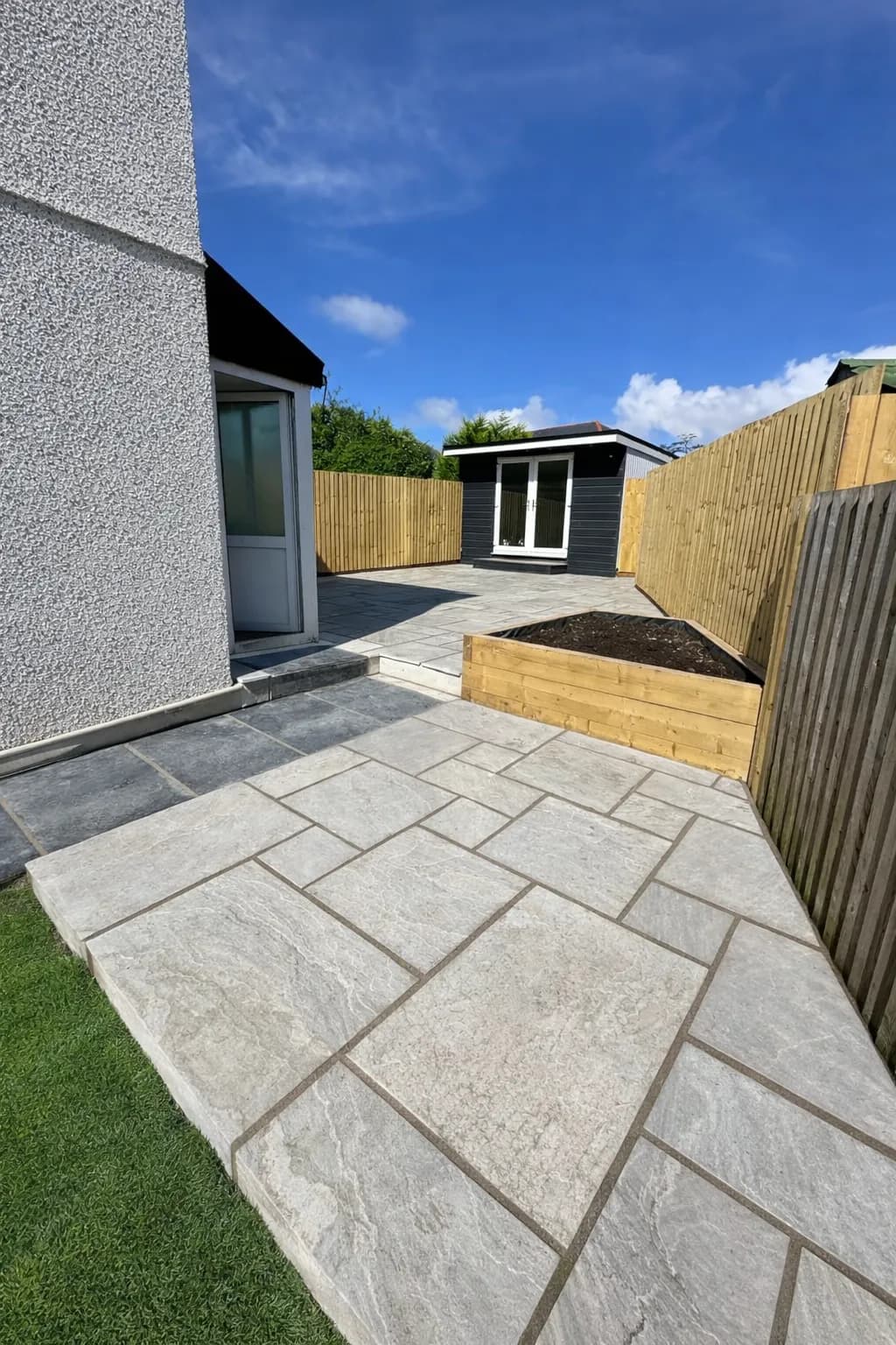 Light grey Indian sandstone patio laid in a random pattern with contrasting dark border at rear of property with new fencing and summerhouse.