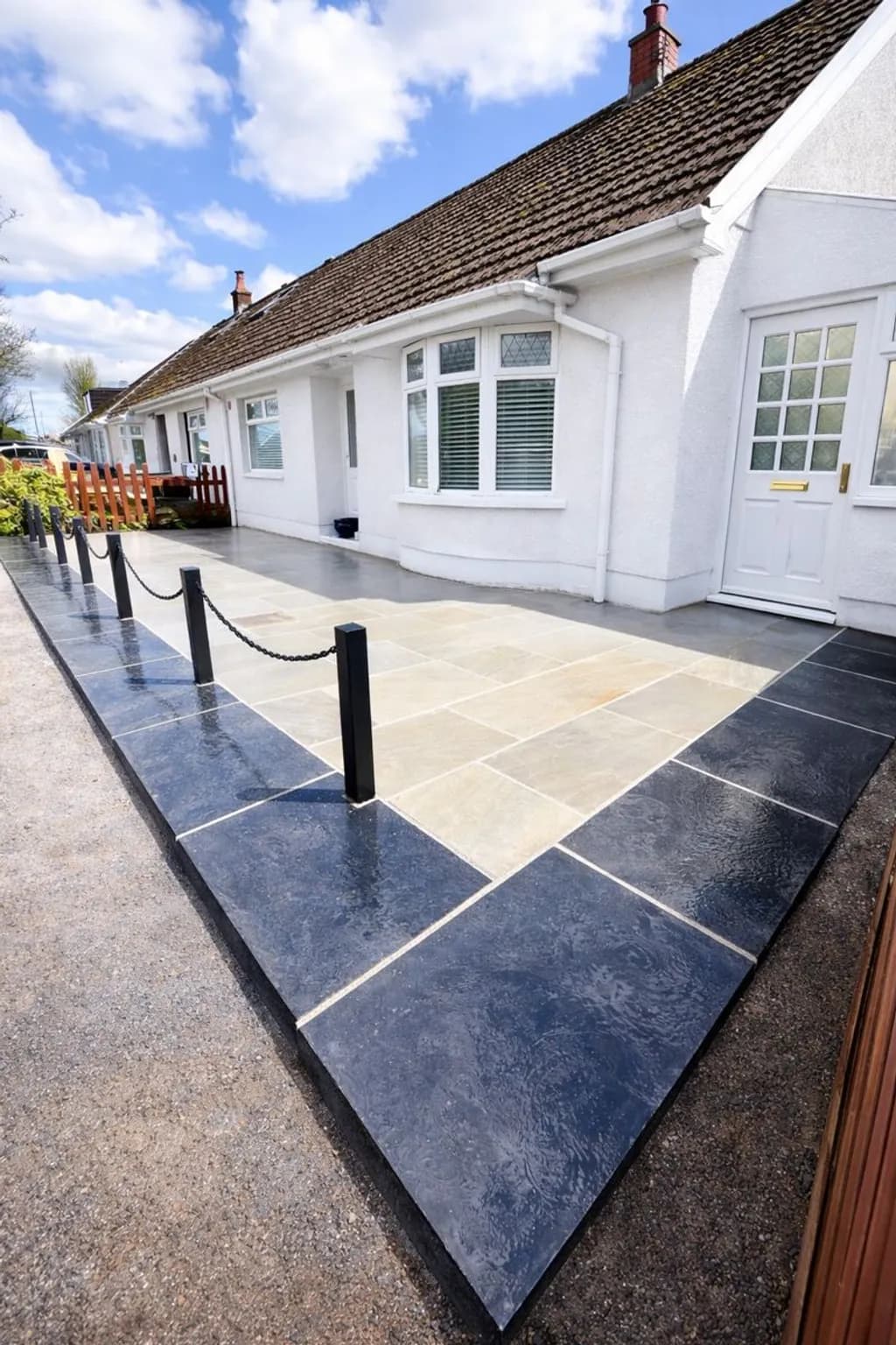 Modern front garden patio installation in Ebbw Vale featuring grey Indian sandstone paving, black limestone edging, and boundary bollards with chains.