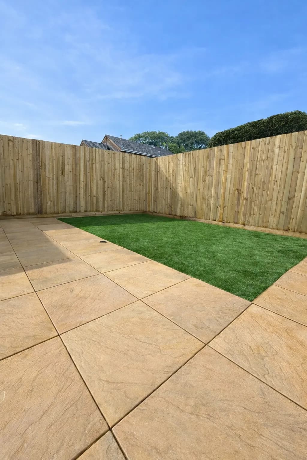 Abergavenny garden renovation showing a single-level layout with fresh patio slabs, low-maintenance artificial grass, and new featheredge fencing with matching gate.